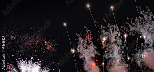 Bright fireworks streaking across dark night sky with glowing trails. 