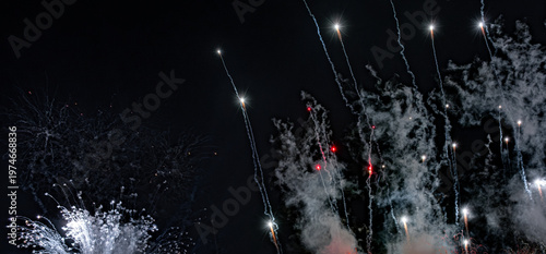 Firework streaks and glowing sparks rising through smoky night sky display. 