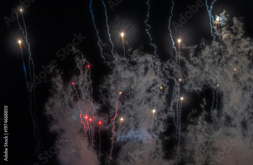 Firework streaks and glowing sparks rising through smoky night sky display. 
