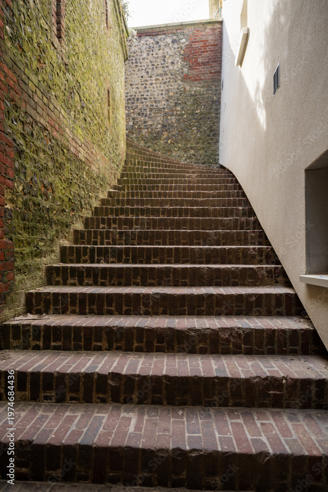 Fototapeta premium Narrow brick staircase between old walls leading upward urban architecture perspective and historic alley concept