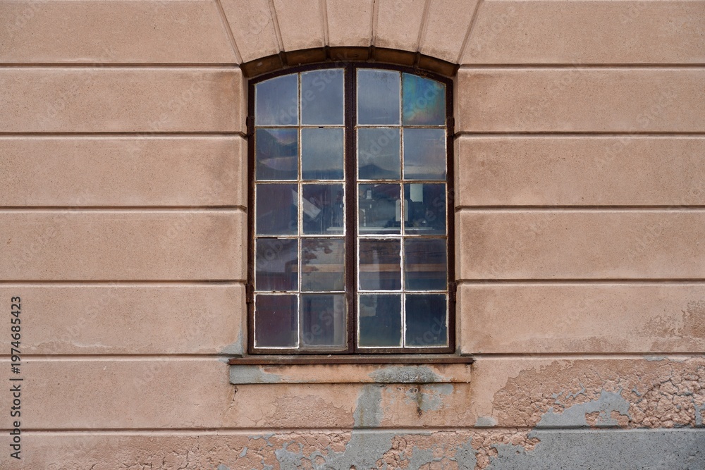 Fototapeta premium A large checkered window with arched top on the worn facade of a building at the navy museum in Horten, Norway.