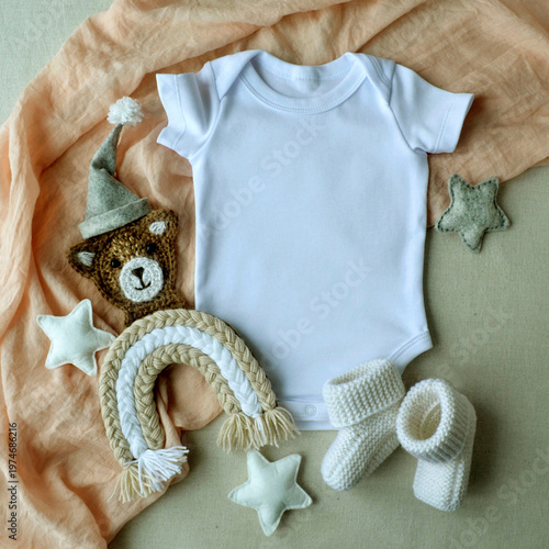 White baby bodysuit mockup with knitted toy bear and booties on fabric textile. Infant clothing design template for apparel shop. Nursery decor accessories with rainbow and star.