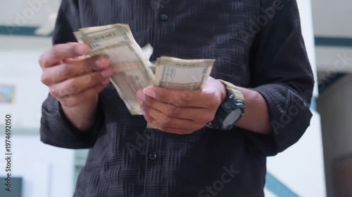 Man in black shirt counting a stack of 500 rupee Indian currency notes