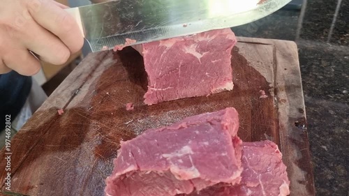 Chef slicing raw beef on a wooden cutting board