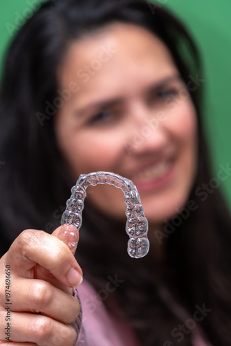 Woman smiling while holding a transparent clear aligner, showcasing invisible braces for teeth straightening and a healthy, confident smile