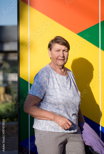 Strong senior woman portrait with colorful wall and dramatic sunlight