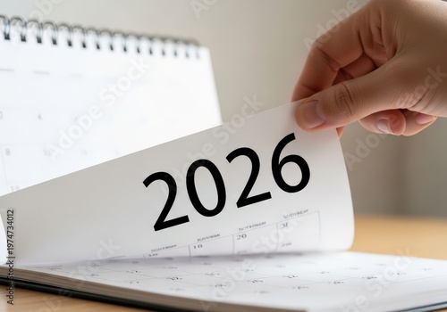A hand turning a page on a desk calendar to reveal the upcoming new year of twenty twenty six.