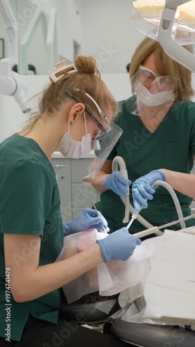 Professional dentist operates ultrasound scaler to eliminate plaque from teeth. Female assistant holds saliva ejector. Routine medical hygiene visit maintains oral health and bright smile