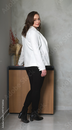 Attractive brunette woman in white blazer and black pants posing in profile, full length indoor portrait with confident elegant style. Office, networking business and face of leadership at startup.