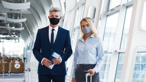 Full length view of the business colleagues of the male and female co-workers standing at the airport with suitcases on wheels and looking at the camera while traveling on the working trip