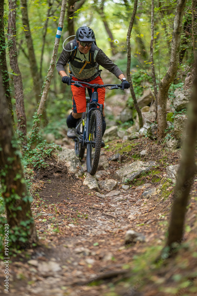 Naklejka premium Mountain biker rides a rocky forest trail wearing helmet and hydration pack