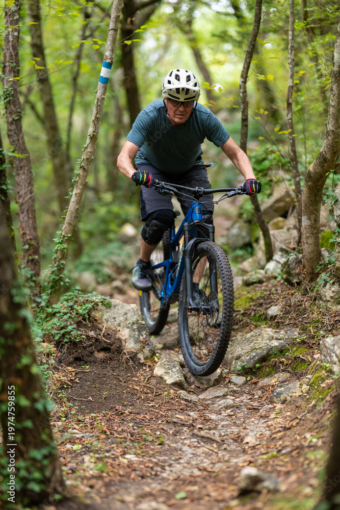 Naklejka premium Man mountain biking on a rocky forest trail wearing helmet and protective gear