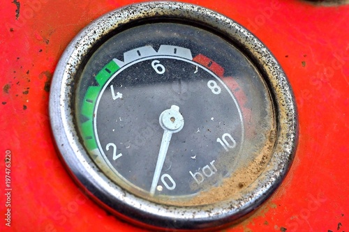 Close-up of a vintage analog pressure gauge mounted on a tractor with red metal surface.