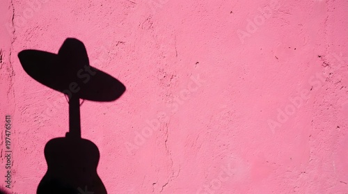 Shadow of an acoustic guitar and a Mexican sombrero on a pink textured wall.