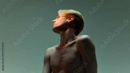 Young man looking up with clean skin in minimal soft lighting background. Concept of anti aging prevention, youthful appearance, collagen care routine, and long term skin maintenance strategy.