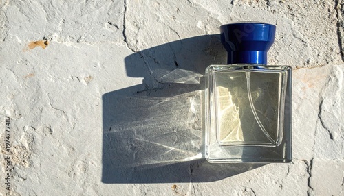Elegant clear glass perfume bottle with blue cap casting shadow on textured surface.