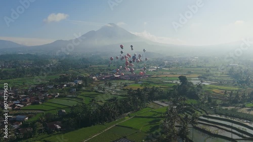 An epic wide aerial view of dozens of hot air balloons ascending gracefully above a vast green valley.Framed by a towering mountain and clear blue sky,the scene captures a breathtaking festival moment