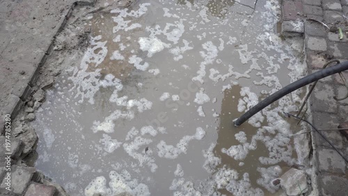 Pumping dirty water with a hose, Sewerage breakthrough, large puddle of muddy water with white foam flowing out of the ground,