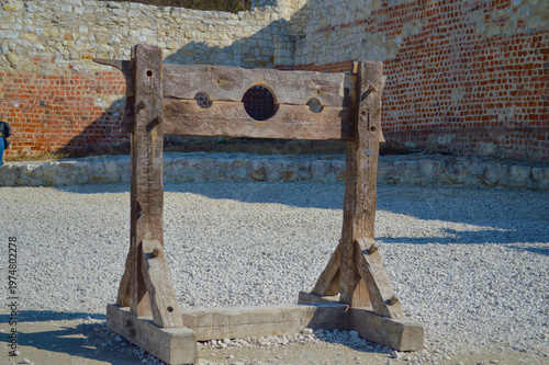 Historical wooden pillory stocks standing in the courtyard of Kazimierz Dolny castle ruins against ancient stone and brick walls in Poland under bright daylight