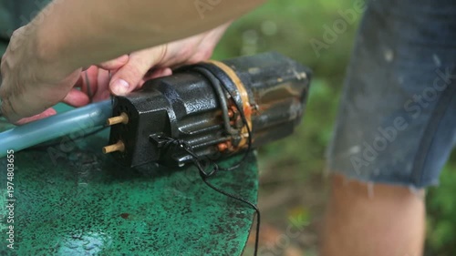 A person uses a tool to fix a blue water hose at an outdoor sink while sunlight shines in the morning hours.