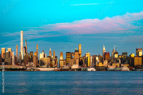 A wide panoramic view across the Hudson River shows the dense architecture of Manhattan during a colorful sunset in New York.