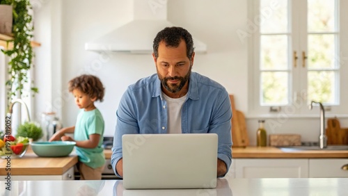 Father Day Man working on laptop in kitchen while child prepares food in background.