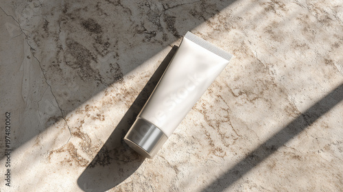 A white tube, likely a cosmetic or skincare product, lies on a textured, light-colored surface with shadows cast across it.