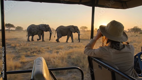 Woman tourist using binoculars to watch elephants from an open top safari jeep in the African savannah.