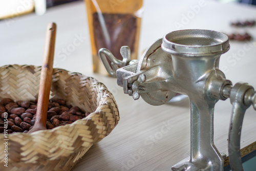 Artisanal chocolate production setup showing cacao beans in a woven basket beside a metal manual grinder, symbolizing traditional craftsmanship and homemade chocolate making