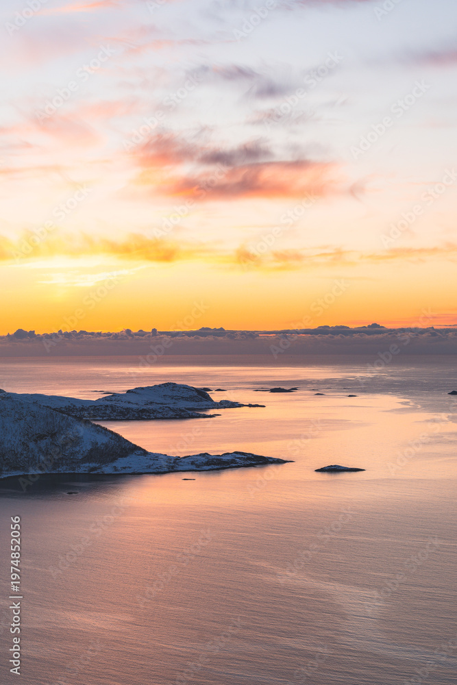 Fototapeta premium Golden sunset over a fjord on Kvaloya, Norway, with sun rays spreading above snow-covered mountains