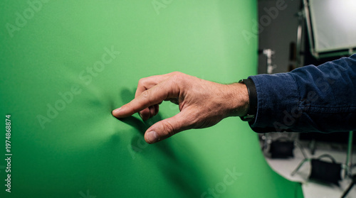 A hand pressing into a vibrant green screen, creating a visible indentation in a studio setting.