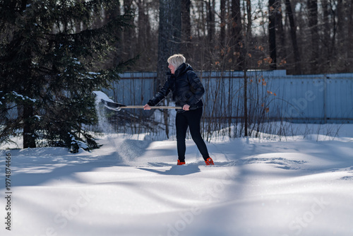 A woman removes snow using a shovel.