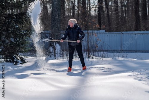 A woman pushes snow off a path.