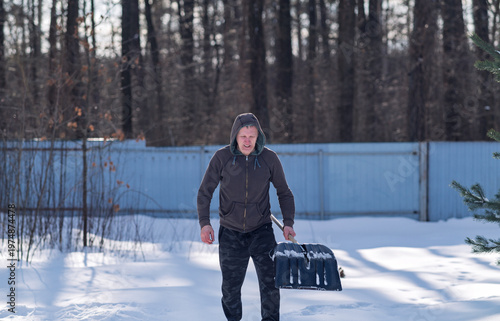 A man in a hoodie holds a snow shovel.