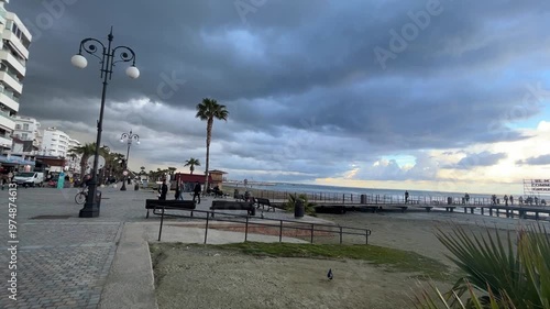 Winter Island. Cloudy coastline, cold sea, sunset, people on the beach. Finikoudes Beach. Larnaca, Cyprus