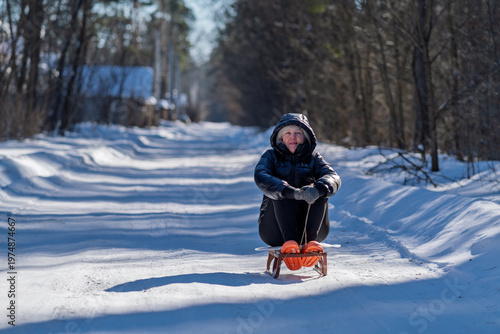 A woman sits on a sled and holds a rope in her hands.