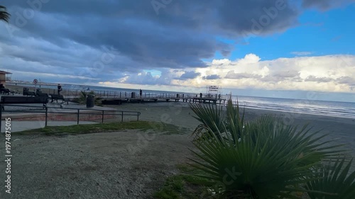 Winter Island. Cloudy coastline, cold sea, sunset, people on the beach. Finikoudes Beach. Larnaca, Cyprus