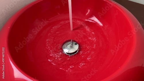 Bathroom red sink, faucet with running water. Saving resources, utility bills. Water resources, water cost