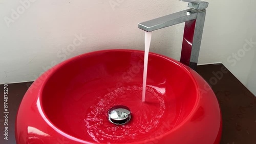 Bathroom red sink, faucet with running water. Saving resources, utility bills. Water resources, water cost