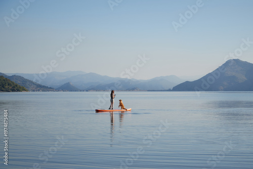 Photos A woman stands with a Nova Scotia Duck Tolling Retriever on a board surrounded by peaceful water