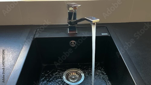 Kitchen black sink, faucet with running water. Saving resources, utility bills. Water resources, water cost
