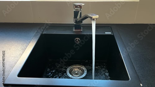 Kitchen black sink, faucet with running water. Saving resources, utility bills. Water resources, water cost