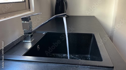Kitchen black sink, faucet with running water. Saving resources, utility bills. Water resources, water cost
