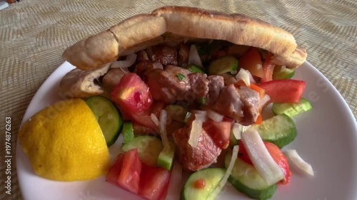 Traditional Greek pork souvlaki in pita bread with grilled vegetables. Tomato and cucumber salad at a Greek gyros taverna.