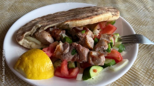 Traditional Greek pork souvlaki in pita bread with grilled vegetables. Tomato and cucumber salad at a Greek gyros taverna.