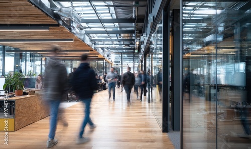Blurred figures walk through a bright, modern office with wood floors