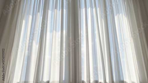 Tall floor-to-ceiling windows covered with flowing white sheer curtains, soft sunlight filtering through, creating gentle shadows