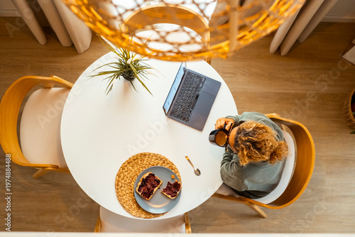 Woman working on a laptop at a round kitchen table with coffee and toast in a cozy home office