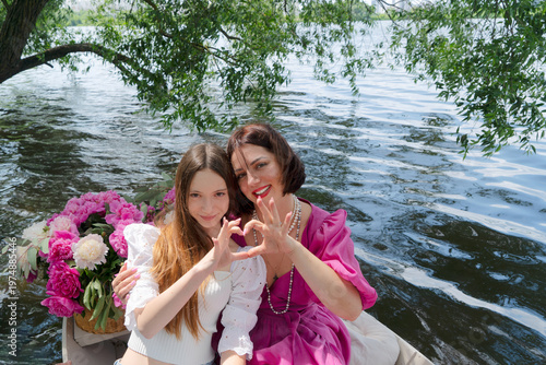 Quadro em tela Caucasian mother and daughter on boat making heart gesture with bouquet of flowe