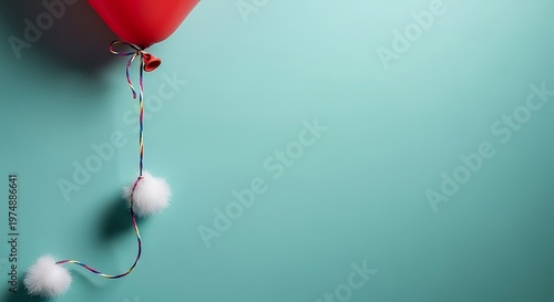 Red balloon with colorful string and white pom poms on teal background